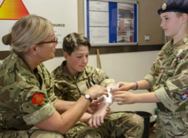 A cadet force adult volunteer helping a cadet with first aid training